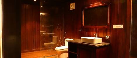 A wooden-paneled bathroom with a toilet, shower, and sink.