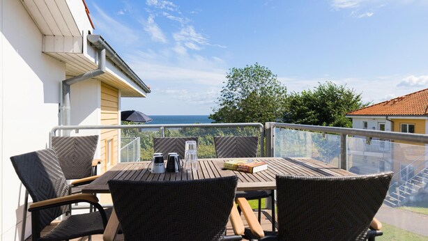 A wooden deck with a table and chairs, overlooking a scenic view of the sea and greenery. - Gudhjem Søpark Lejl. 46 (Gudhjem)