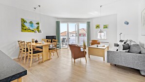A modern living room with a dining area, a sofa, and a TV. - Gudhjem Søpark Lejl. 46 (Gudhjem)