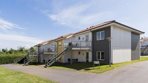 A two-story residential building with a balcony on the upper floor, a staircase leading to the entrance, and a sign indicating the building number. - Gudhjem Søpark Lejl. 46 (Gudhjem)