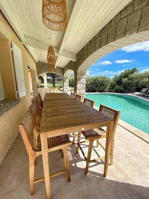 A wooden table with chairs in an outdoor area with a pool view. - Maison Pour 12 Personnes, 5 ch, 1ha de Terrain Sans Vis-à-vis, Piscine Chauffée (Ruoms)