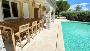 A poolside area with a wooden table and chairs, stone pillars, and a clear blue pool.