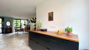A modern kitchen with a stone tile floor, a wooden countertop, and black cabinets. There is a dining area with a table and chairs visible in the background. - AMSTERDAM TOWN HOUSE WITH PRIVATE GARDEN & PARKING (Amsterdam)