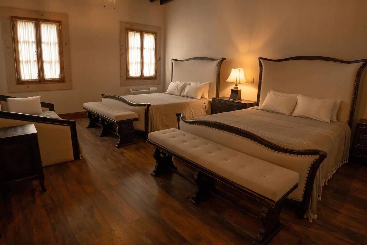 Habitación de hotel con dos camas individuales, un banco, un escritorio y una mesita de noche con lámpara.