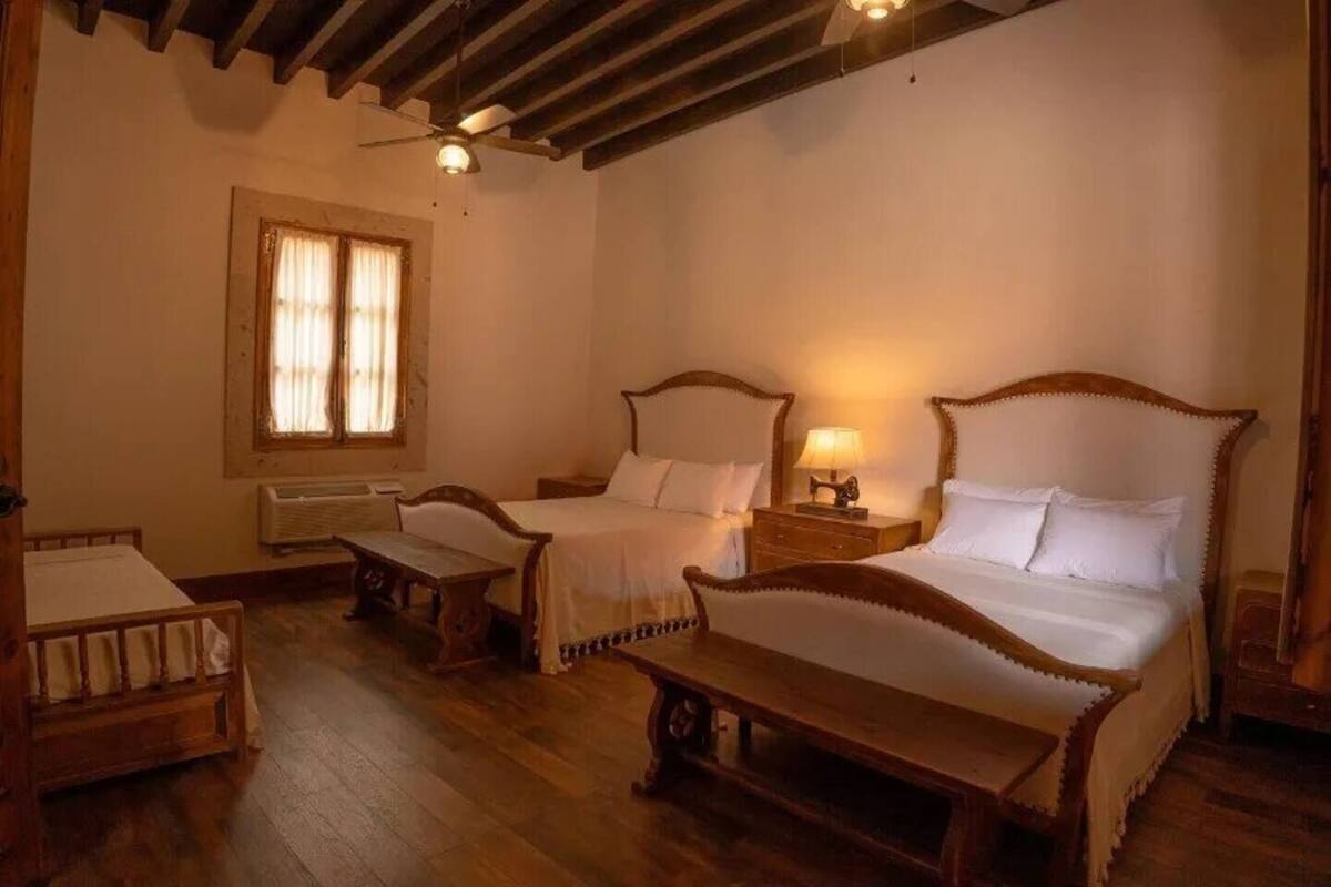 Una habitación tradicional con dos camas de madera, un banco y una ventana con cortinas.
