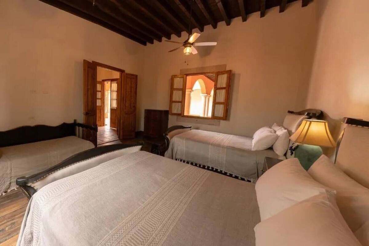 Habitación de hotel con dos camas, ventilador de techo y ventana con persianas de madera.