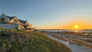 Una casa costera con balcón que da al mar, cielo despejado y el sol poniéndose o saliendo.
