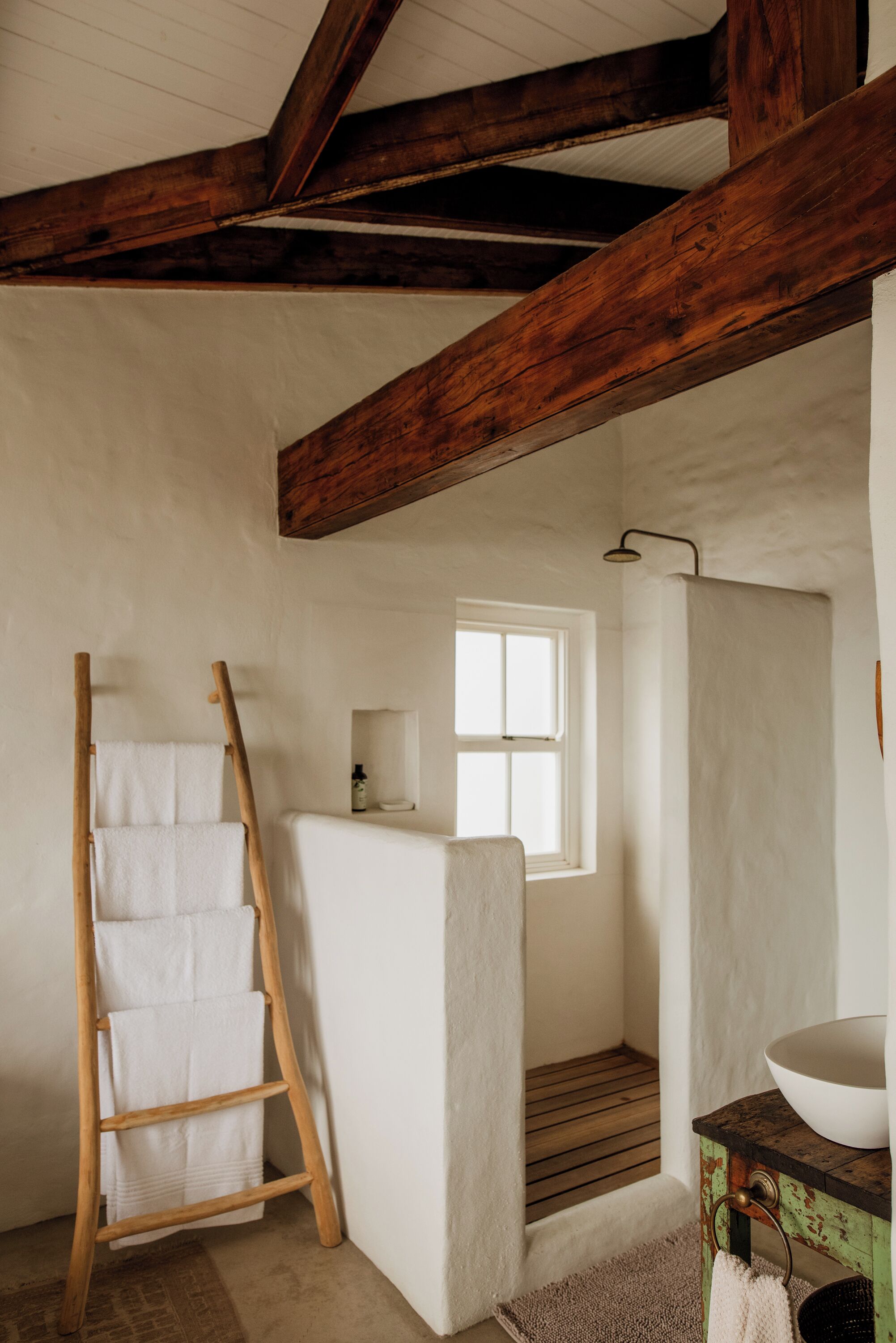 A rustic bathroom with a wooden ladder, a shower, and a basin.