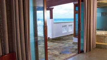 A room with a glass door leading to a balcony with a view of the ocean.