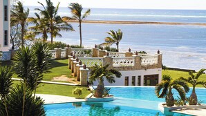 Una piscina con vistas al océano, rodeada de palmeras y un edificio de fachada blanca.
