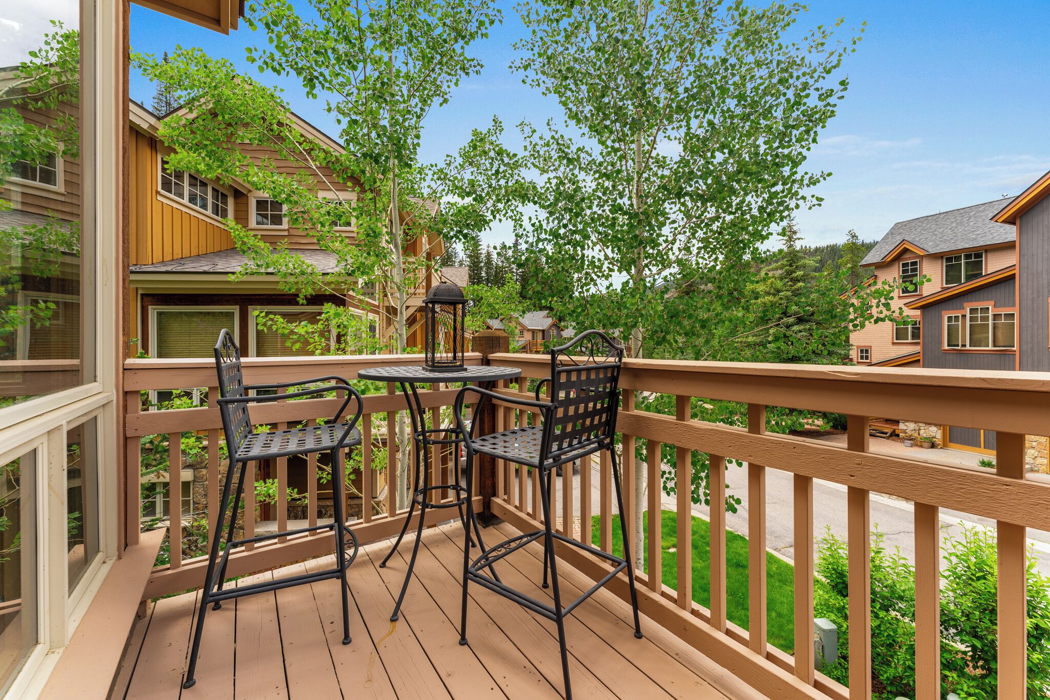A wooden deck with two metal chairs and a table, surrounded by a wooden railing.