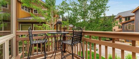 A wooden deck with two metal chairs and a table, surrounded by a wooden railing.