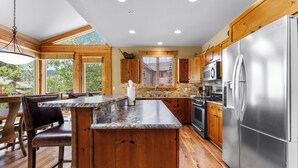 A spacious kitchen with wooden cabinets, a stainless steel refrigerator, and a large island with seating. - Luxurious and Comfy Townhome w/ 2 Balconies & Patio w/ Mountain Views! (Keystone)