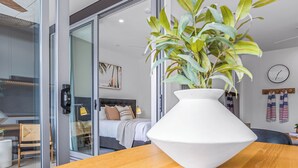 Moderni hotellihuone, jossa on suuri ikkuna, sängynpääty, yöpöytä ja ruukussa oleva kasvi.