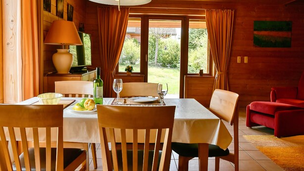 A wooden dining room with a table set for two, chairs, a lamp, and a view of the garden. - Find With Nr 509 Your Holiday Home in the Harz Mountains (Oberharz am Brocken)