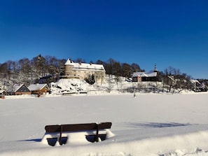 A snow-covered landscape with a large building on a hill, a smaller structure with a steeple, and a bench in the foreground. - Find With Nr 509 Your Holiday Home in the Harz Mountains (Oberharz am Brocken)
