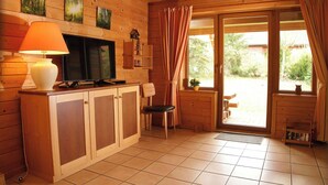 A wooden cabin interior with a kitchen area, a television, a lamp, and a sliding glass door leading to an outdoor patio. - Find With Nr 509 Your Holiday Home in the Harz Mountains (Oberharz am Brocken)