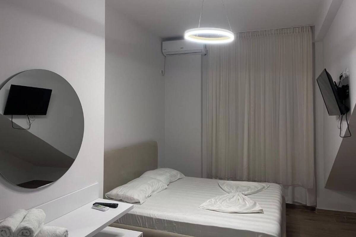 Une chambre d’hôtel moderne équipée d’un lit, d’un miroir rond, d’un téléviseur à écran plat, d’un bureau avec une télécommande et d’un téléviseur fixé au mur.