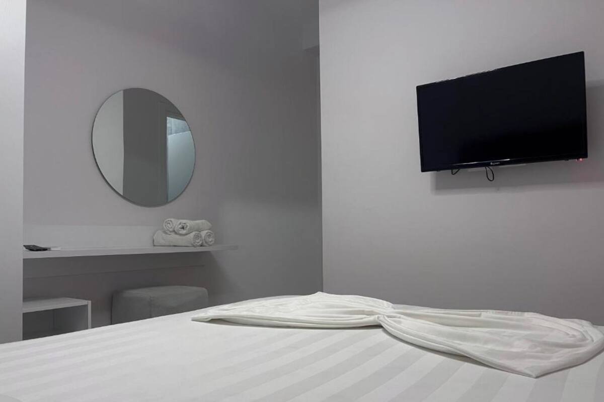 Une chambre d’hôtel avec un lit, un miroir rond, un téléviseur à écran plat et un porte-serviettes.