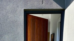 A modern entrance with a wooden door, a small potted plant, and a metal grate. - Peaceful retreat 6 km north of Coffs Harbour! (Korora)