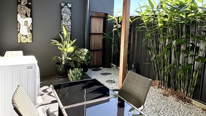 A modern outdoor seating area with a glass-top table and wicker chairs, surrounded by potted plants and a bamboo fence. - Peaceful retreat 6 km north of Coffs Harbour! (Korora)