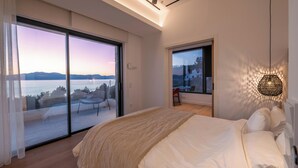 A modern bedroom with a large bed, a balcony with a view of the sea, and a dining area with a view of the mountains. - Elia Cove Luxury Villas & Residences (Loutraki-Agioi Theodoroi)