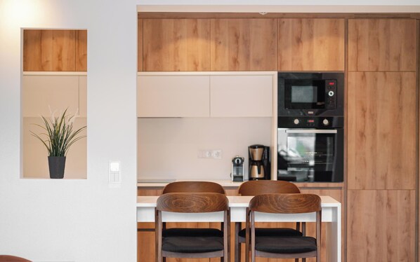 A modern kitchen with wooden cabinets, a microwave, an oven, and two chairs at a white table.