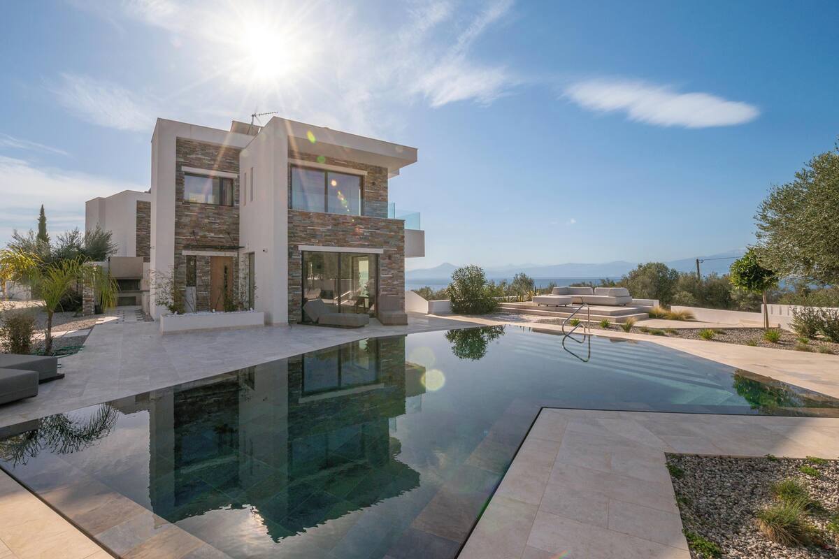 A modern two-story house with a swimming pool, outdoor seating, and a view of the mountains.