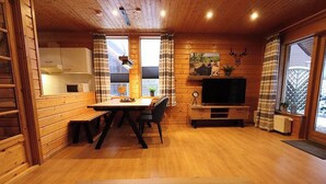 A cozy cabin interior with a wooden dining table, chairs, a television, and a kitchen area. - The House to Stay for Holidays (Oberharz am Brocken)
