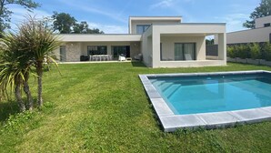 Une maison moderne dotée d’une piscine, d’un patio avec mobilier d’extérieur et d’une pelouse bien entretenue.