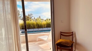Une chambre avec un lit, une chaise et une vue sur une piscine et la verdure environnante.