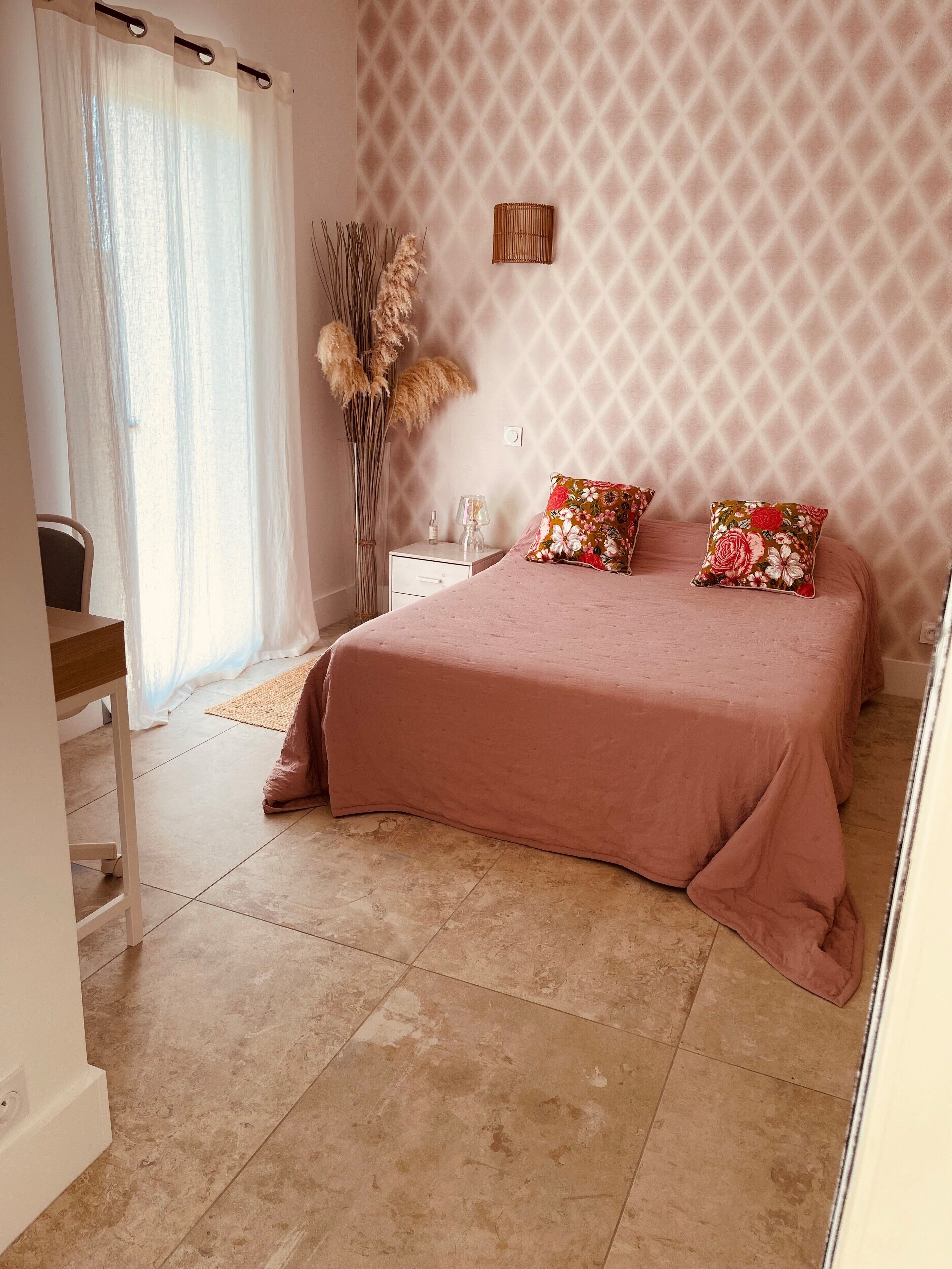 Una camera da letto con un letto, un comodino, una lampada, un vaso con piante essiccate e una finestra con tende.