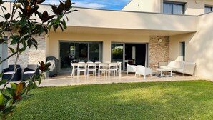 Une terrasse extérieure moderne, dotée d’un espace repas, de sièges et offrant une vue sur la verdure environnante.