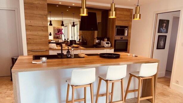 Une cuisine moderne dotée d’un îlot central, de tabourets de bar, de luminaires suspendus et d’un four à micro-ondes.