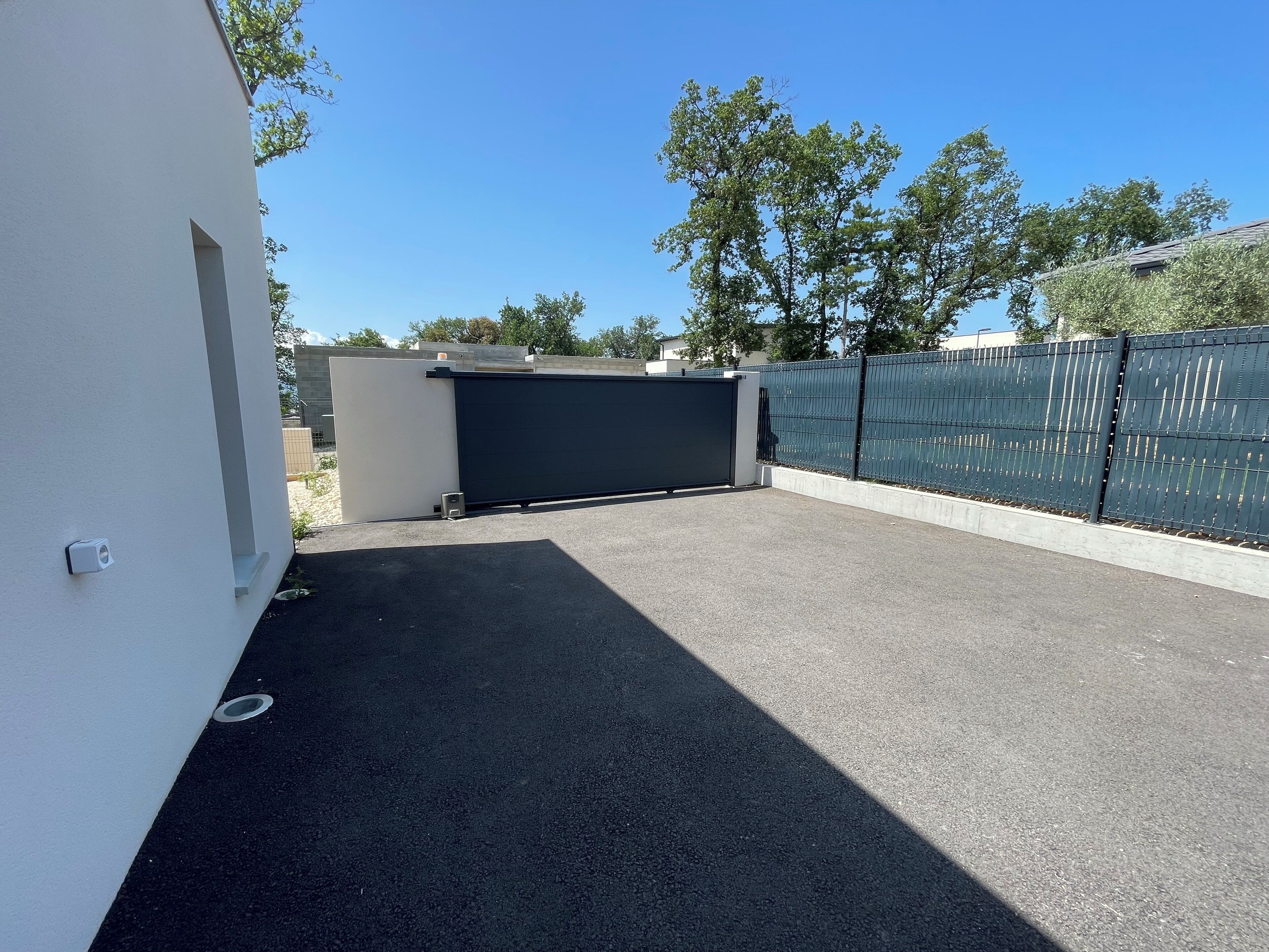 Una terraza en la azotea con un portón cerrado, una pared blanca y una valla metálica.