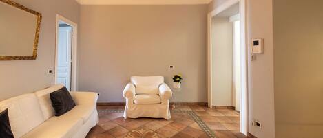 A living room with a white sofa, a white armchair, and a patterned floor.