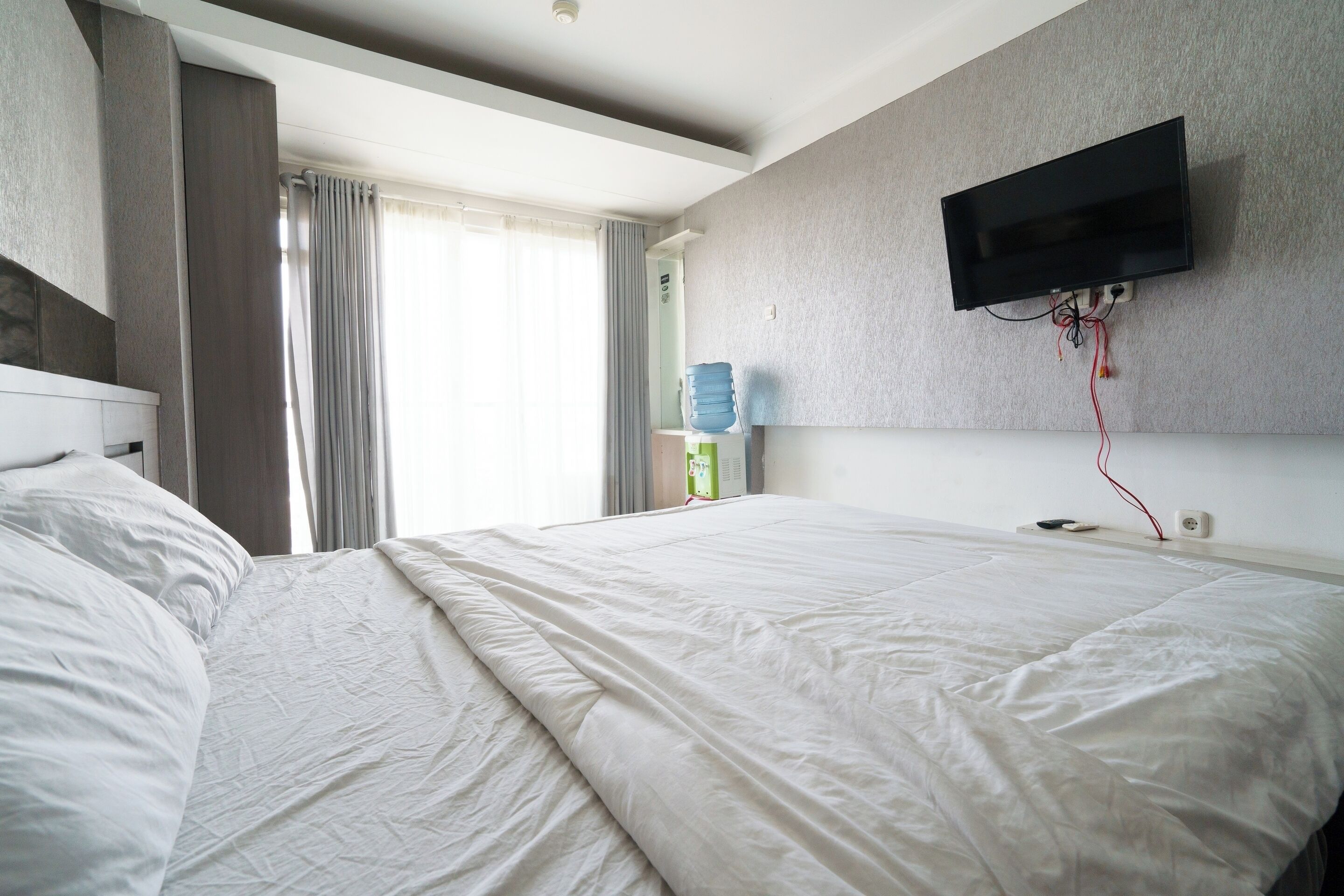 Une chambre d’hôtel avec un grand lit, un téléviseur à écran plat fixé au mur et un distributeur d’eau sur le côté.