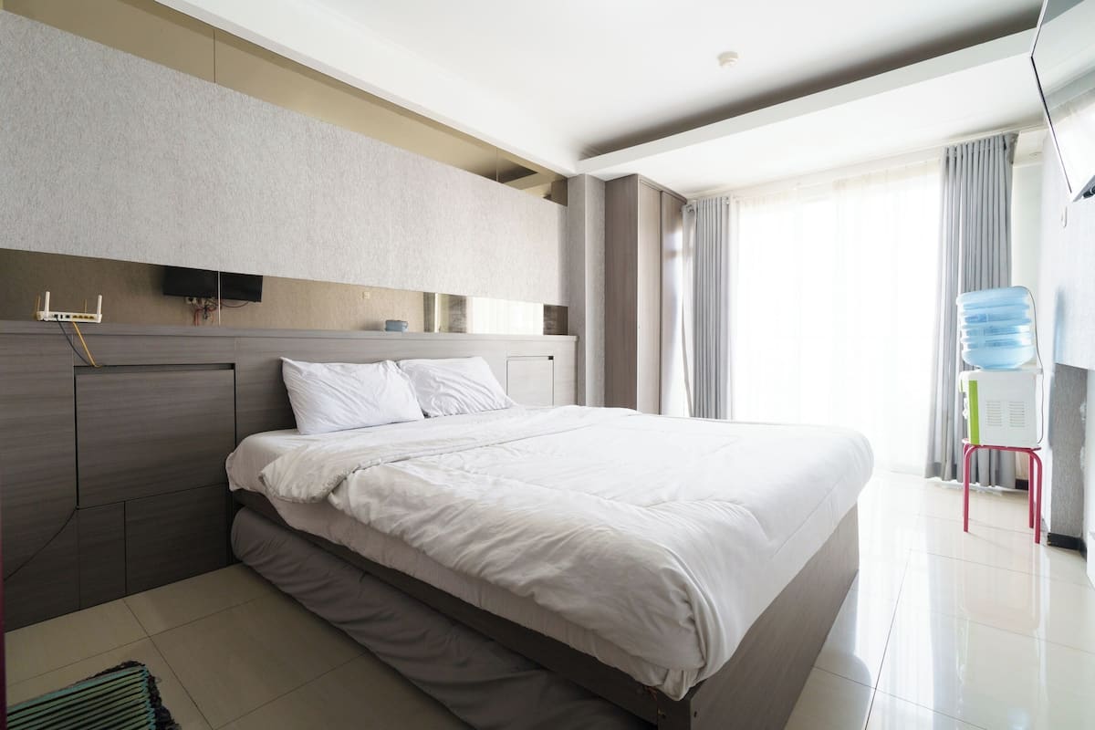 Una habitación de hotel moderna con una cama grande, un televisor de pantalla plana montado en la pared y un dispensador de agua.