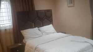 Een slaapkamer met een bed, nachtkastje, airconditioning en een raam met gordijnen.
