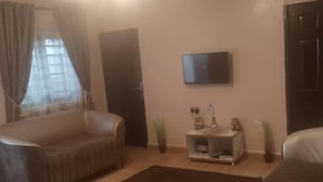 Een woonkamer met een bank, een salontafel, een aan de muur bevestigde televisie en een deur.