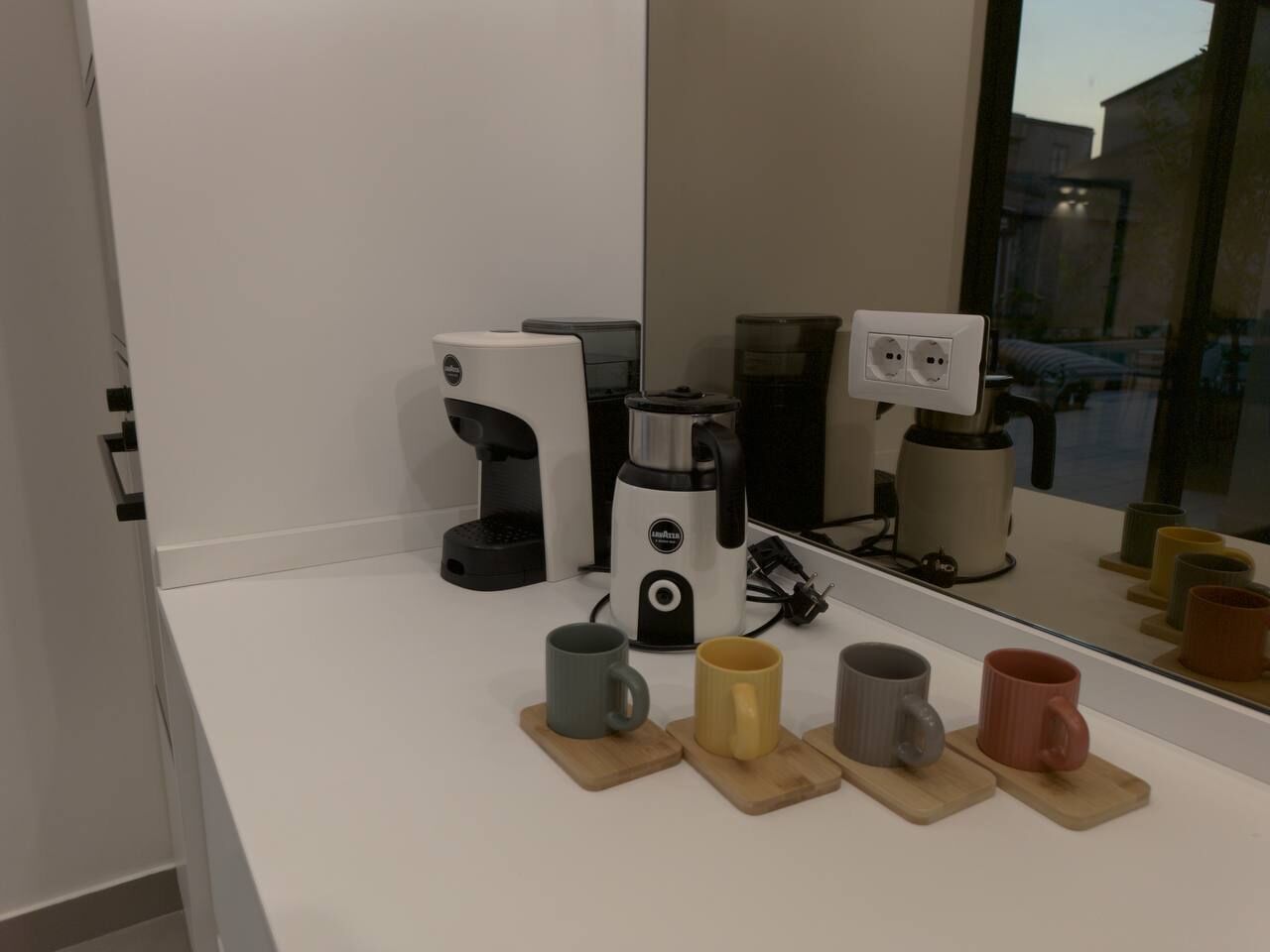 A kitchen counter with a coffee maker, a blender, and a coffee machine. There are four mugs on wooden coasters.