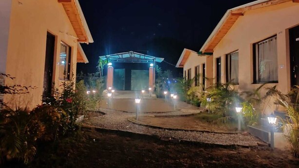A hotel entrance with a covered walkway, illuminated by ground lights, and surrounded by vegetation. - The Jungle Hideout Jim Corbett (Ramnagar)