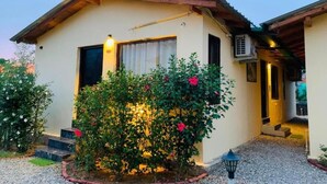 A two-story building with a beige facade, a wooden roof, and a small garden with flowering bushes. - The Jungle Hideout Jim Corbett (Ramnagar)