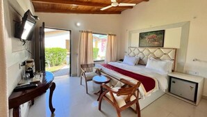 A bedroom with a bed, a desk, a chair, a small table, a ceiling fan, and a TV. - The Jungle Hideout Jim Corbett (Ramnagar)