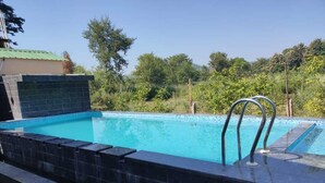 A swimming pool with a tiled edge, a stone wall, and a metal ladder. - The Jungle Hideout Jim Corbett (Ramnagar)