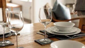 Une table à manger dressée avec des assiettes, des verres et des couverts, avec une table en bois et une chaise en arrière-plan.