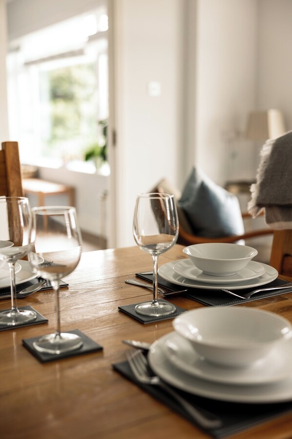 A dining table set with plates, glasses, and cutlery, with a wooden table and a chair in the background.