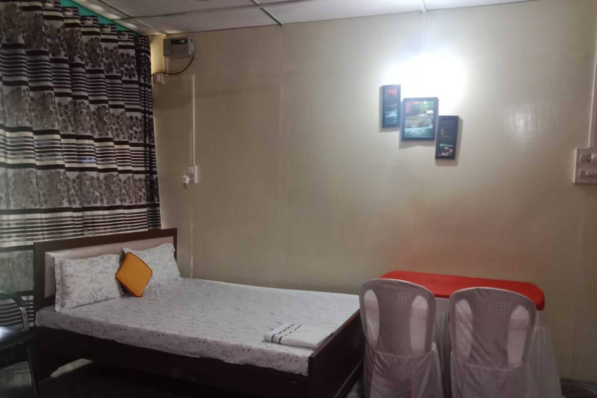 Ein Hotelzimmer mit einem Bett, einem kleinen Tisch, zwei Stühlen, einer Wand mit einem gemusterten Vorhang und einer wandmontierten Klimaanlage.