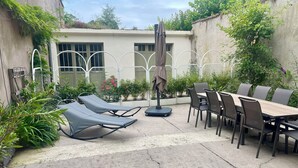 Eine Terrasse mit Esstisch und Stühlen, umgeben von Topfpflanzen und einem Schaukelstuhl.