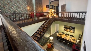 Ein mehrgeschossiges Interieur mit Treppe, einer Kandelaberleuchte, einem Essbereich und Wandtapete mit Muster.